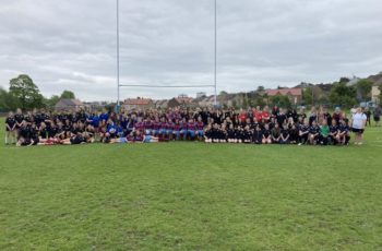 150 young people with their teachers standing in a group on a rugby field.