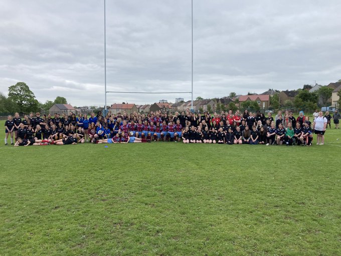 150 young people with their teachers standing in a group on a rugby field.
